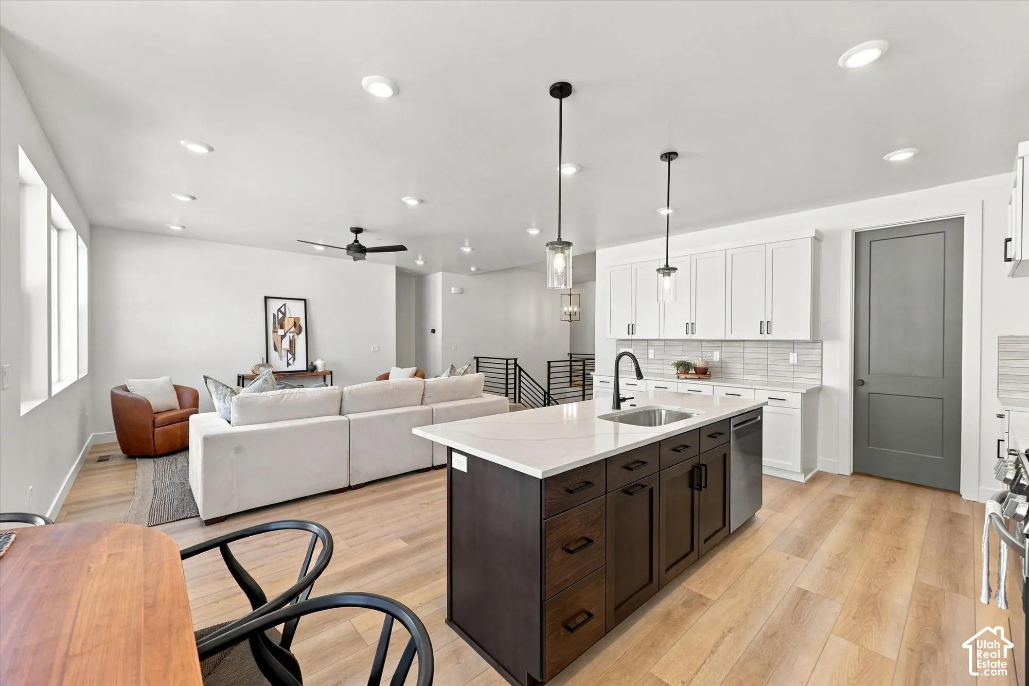 Kitchen featuring a contrasting center island with a stone countertop and undermount sink, white upper cabinetry, light-toned wood-finish flooring, and recessed ceiling lighting