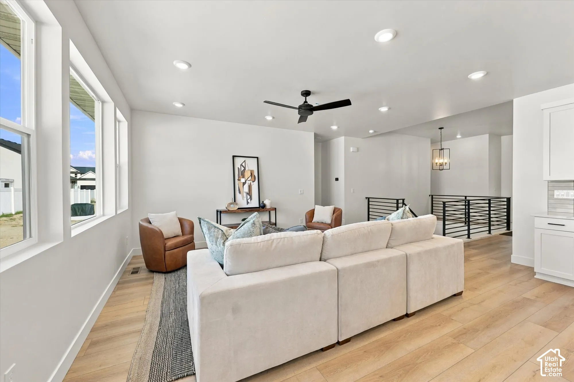 Open-concept interior featuring wood-finish flooring, recessed lighting, a matte black ceiling fan, expansive windows, and a metal horizontal-bar railing