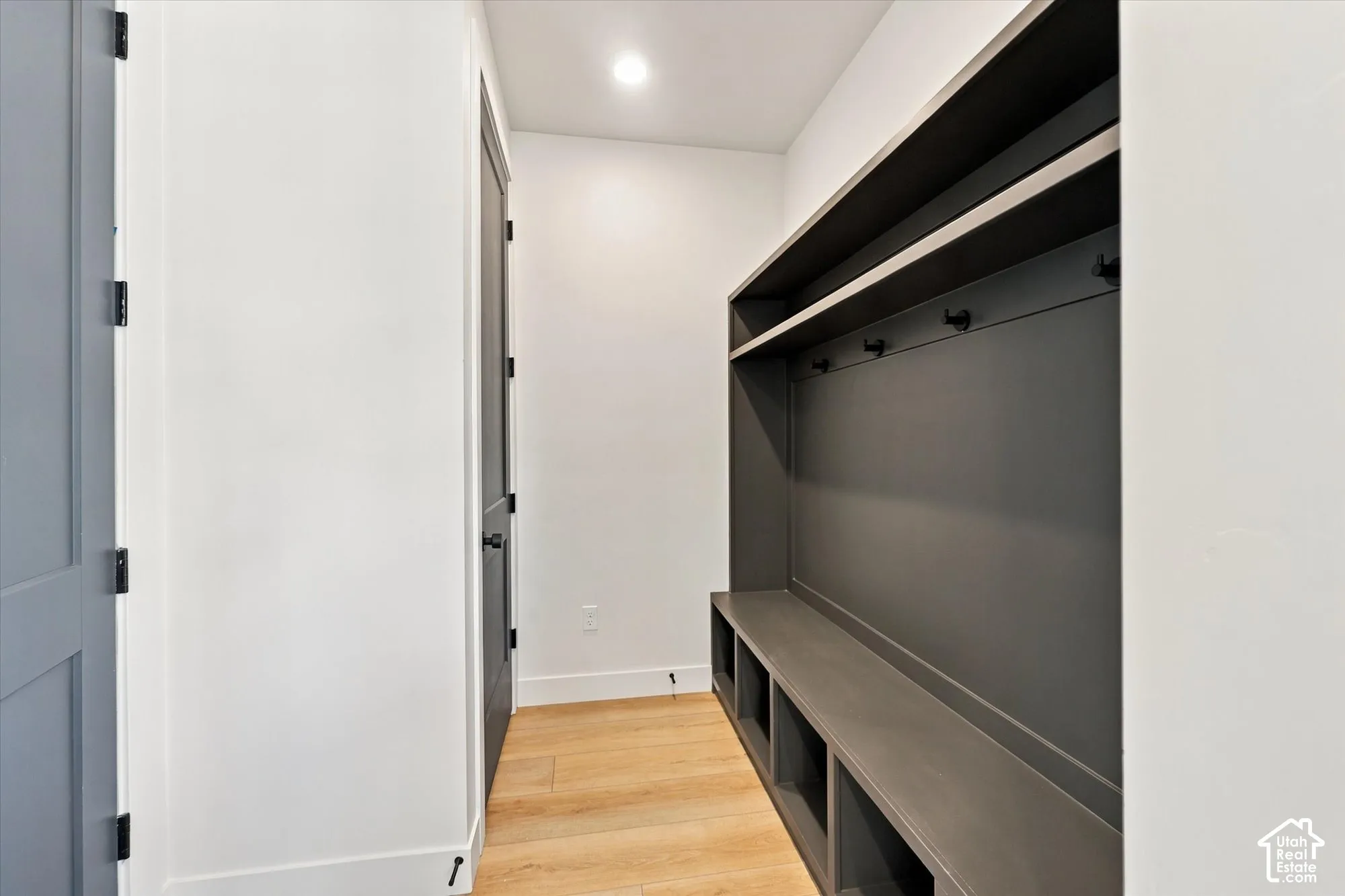 Built-in charcoal cabinetry featuring open shelving, a bench seat, and matte black hardware, complemented by light wood-finish flooring and recessed lighting