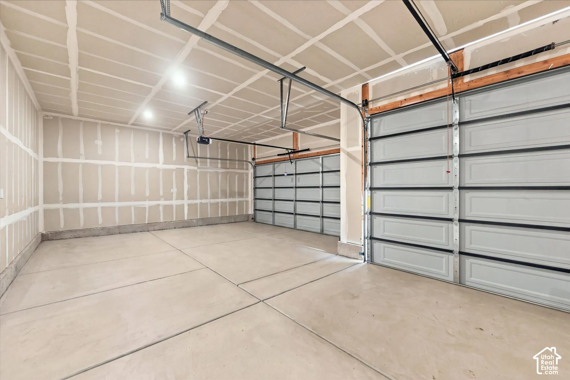 Multi-vehicle garage featuring concrete flooring, two overhead sectional doors, and exposed taping on drywall ceiling and walls