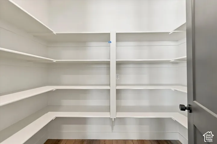 Walk-in pantry featuring white wrap-around tiered shelving, shiplap-style wall detailing, and wood-finish flooring