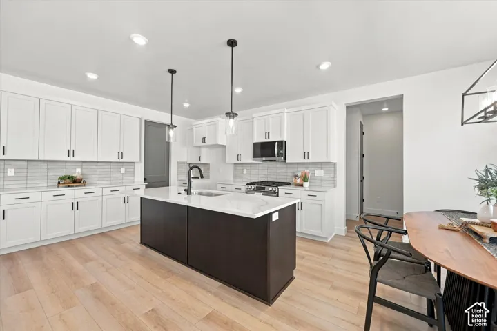 Kitchen featuring white cabinetry, a contrasting dark-toned center island with a stone-finish countertop, stainless steel appliances, linear tile backsplash, and wood-finish flooring