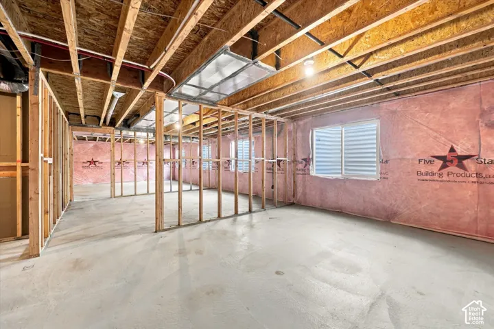 Unfinished lower level featuring exposed wood framing, concrete flooring, installed pink batt insulation, and sliding egress windows