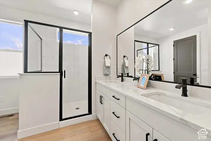 Dual-sink vanity with quartz countertops, white shaker-style cabinetry, matte black hardware, glass-enclosed shower with black frame, and large wall-mounted mirror