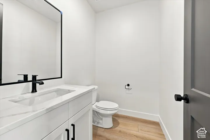 White cabinetry with solid-surface countertop, rectangular undermount sink, matte black faucet, wall-mounted mirror with black frame, and wood-finish flooring