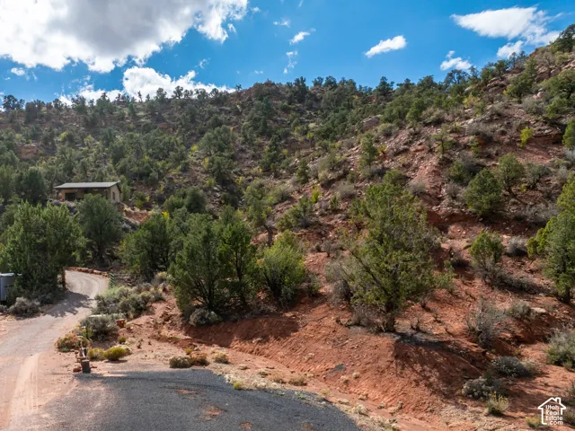 Rugged desert terrain featuring red rock formations, native vegetation, and a paved driveway leading to an expansive site