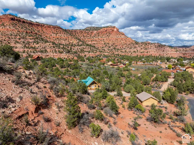 Aerial perspective of a multi-level residence featuring a pitched metal roof, expansive glass windows, and natural desert surroundings with prominent red rock formations