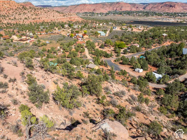 Aerial perspective featuring high-desert terrain, native vegetation, rock formations, and regional red rock topography