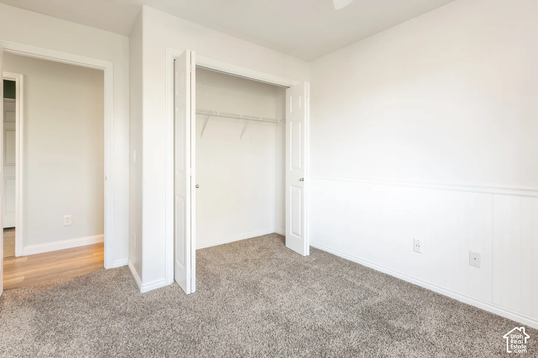 Room featuring carpeted flooring, white wainscoting, and a built-in closet with bifold doors