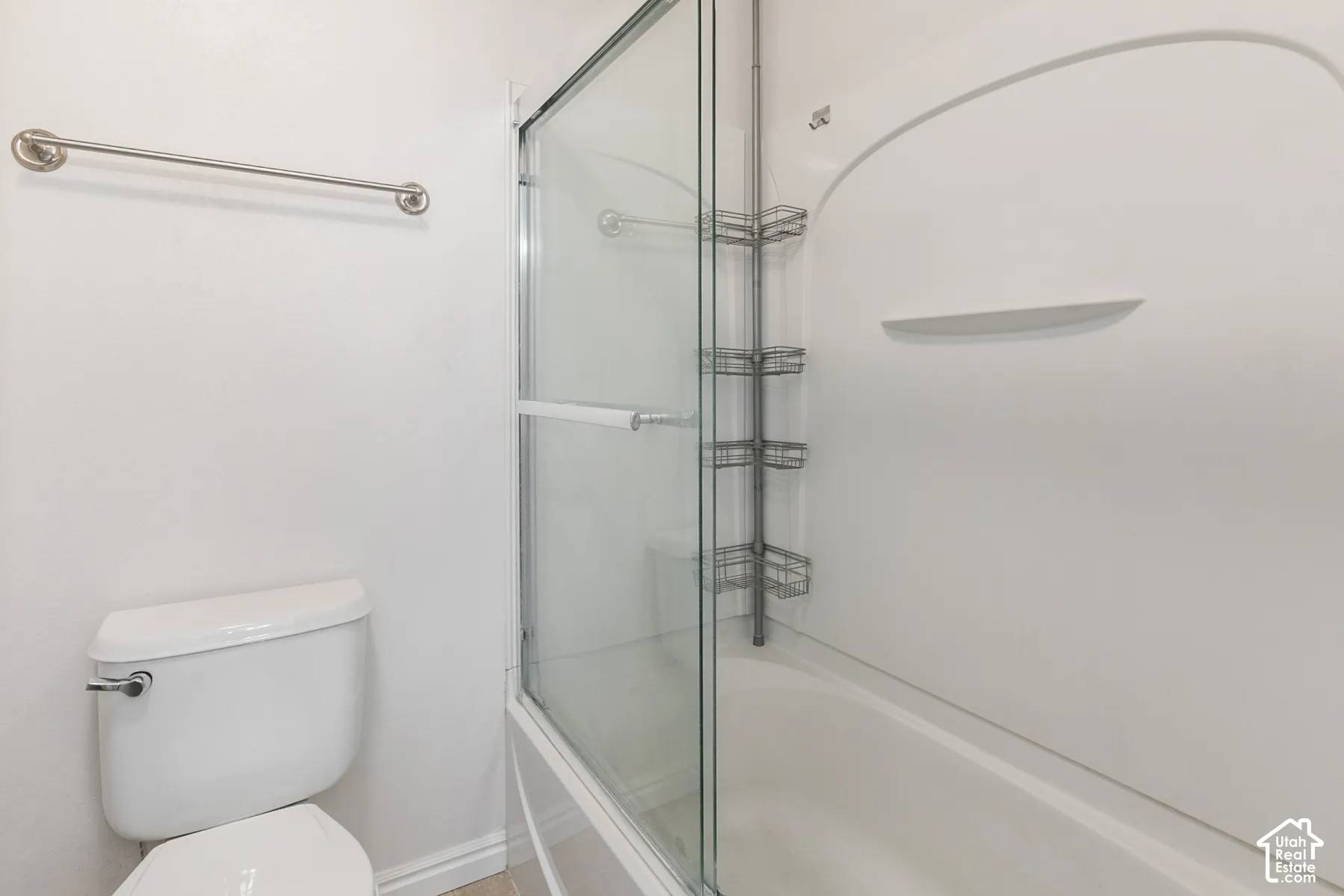 Bathroom featuring a white porcelain toilet, a molded acrylic tub surround with integrated shelving, and a glass sliding shower enclosure with polished chrome hardware