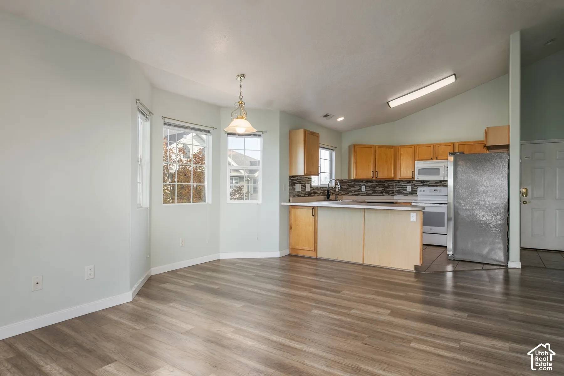Vaulted ceilings, wood-finish flooring, bay windows, kitchen peninsula with breakfast bar, and tile backsplash