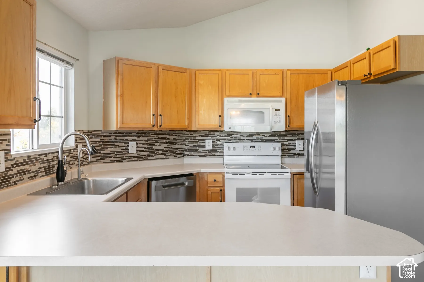Kitchen featuring light wood cabinetry, stone-tiled backsplash, stainless steel appliances, and a peninsula countertop