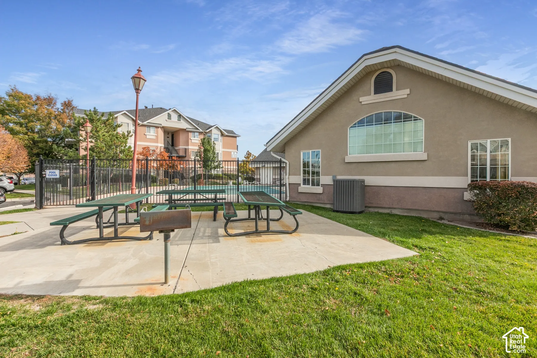 Outdoor common area featuring a concrete patio, built-in metal grill, multiple picnic tables, and metal perimeter fencing