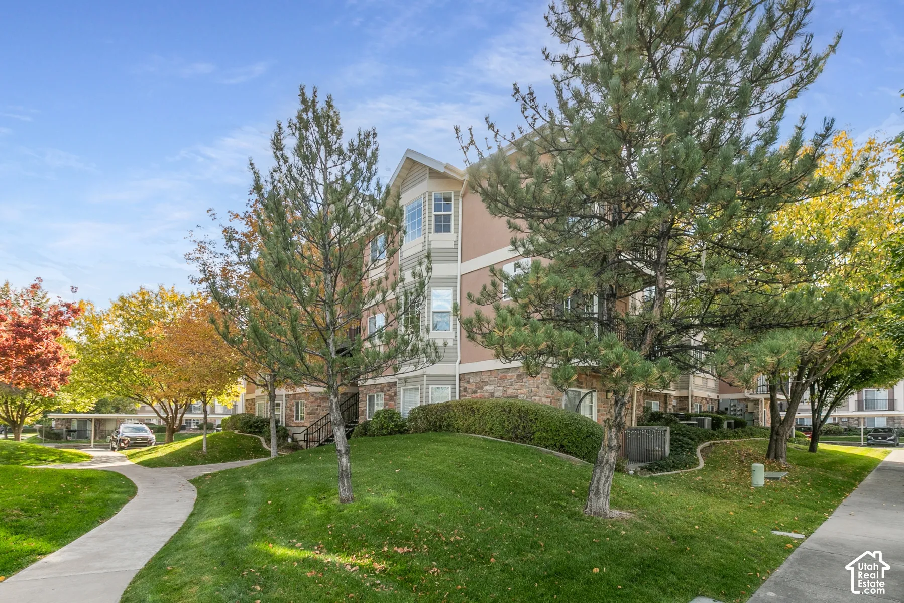 Multi-story exterior featuring stone veneer siding, stucco accents, and integrated balconies surrounded by mature landscaping and concrete walkways