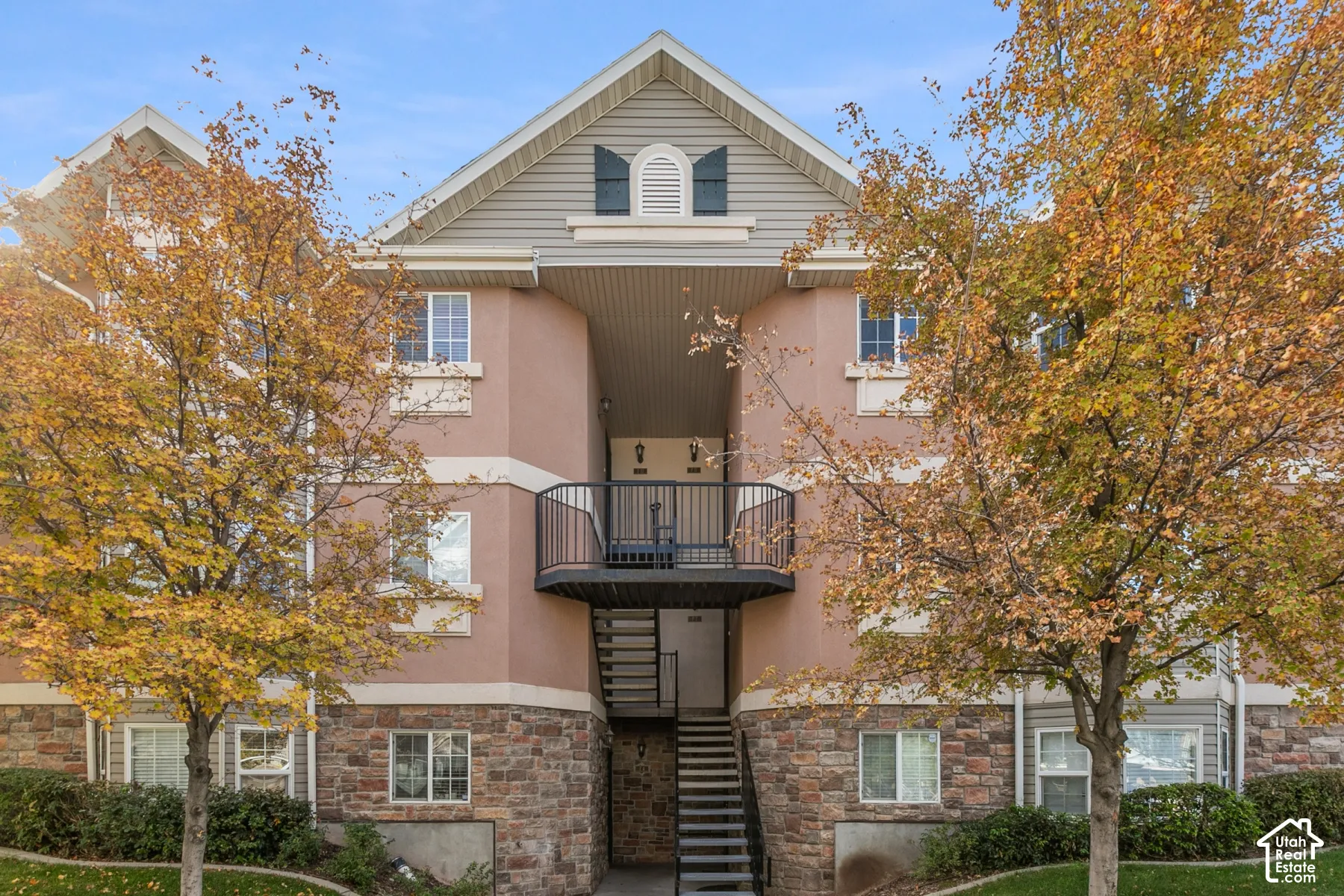 Multi-story exterior featuring stone veneer siding, horizontal siding gables, decorative shutters, and a private metal balcony