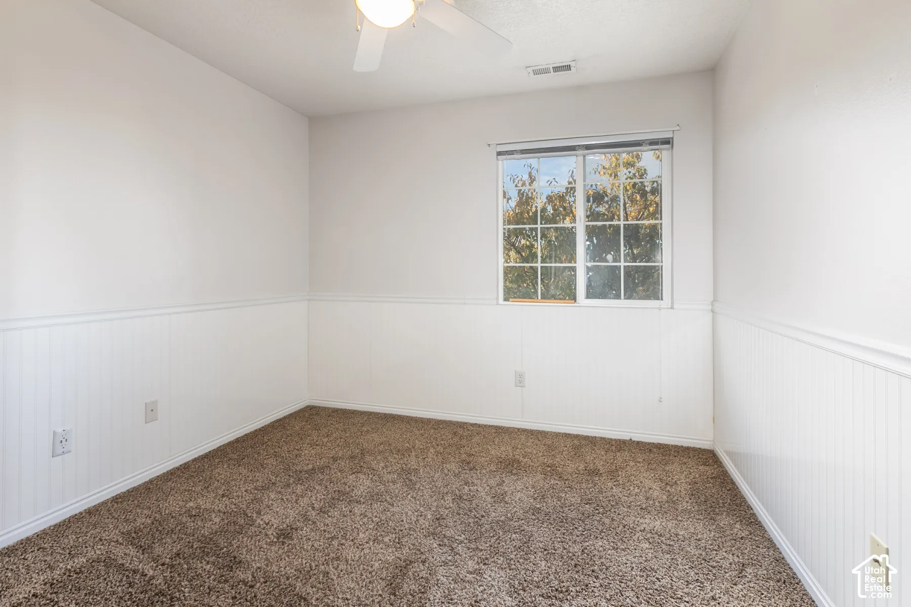 Room interior featuring white beadboard wainscoting, wall-to-wall carpeting, a sliding window with colonial muntins, and a ceiling-mounted light fixture