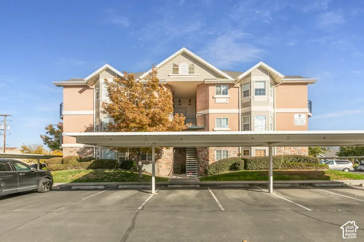 Multi-story building exterior featuring a stone and stucco facade, gabled rooflines, decorative shutters, and covered parking structures
