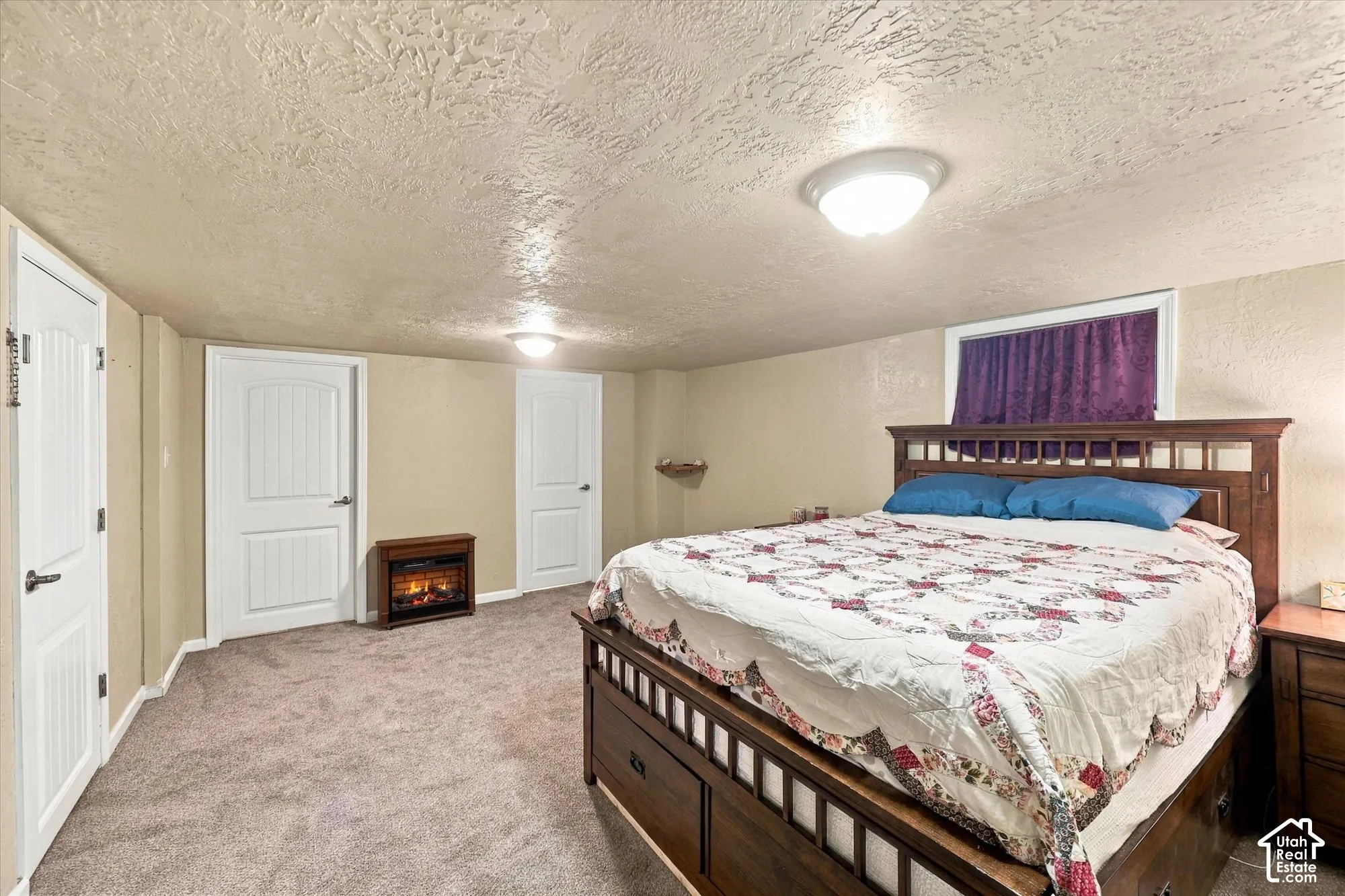 Interior space featuring neutral wall-to-wall carpeting, textured ceiling, two panel-style doors, and a built-in electric fireplace unit