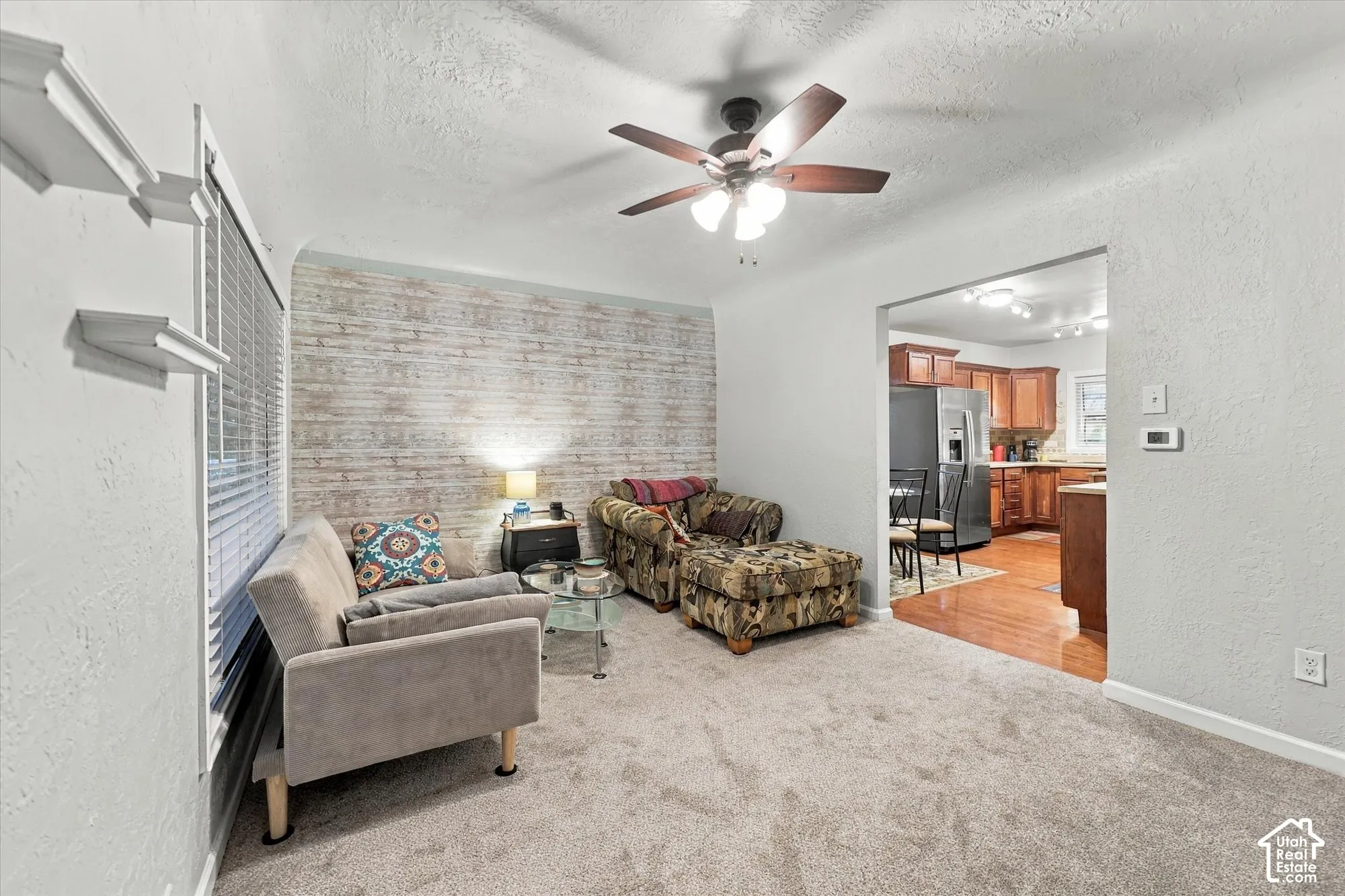 Textured wall finish with decorative patterned accent wall, neutral carpeting, ceiling fan with multi-light fixture, and built-in wall shelving