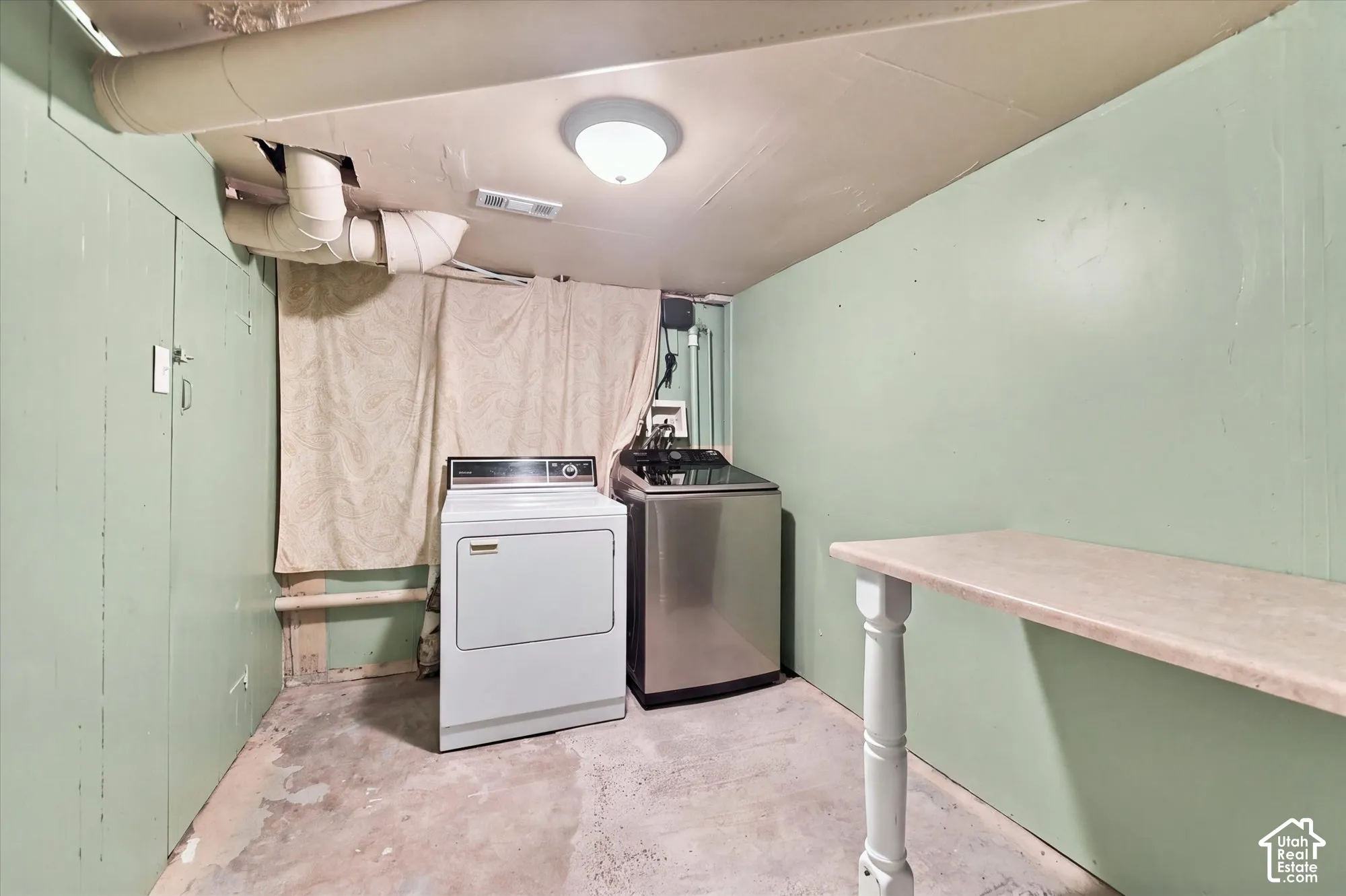 Laundry area featuring a built-in folding counter with a decorative support leg, exposed ceiling infrastructure, flush-mount lighting, and concrete flooring