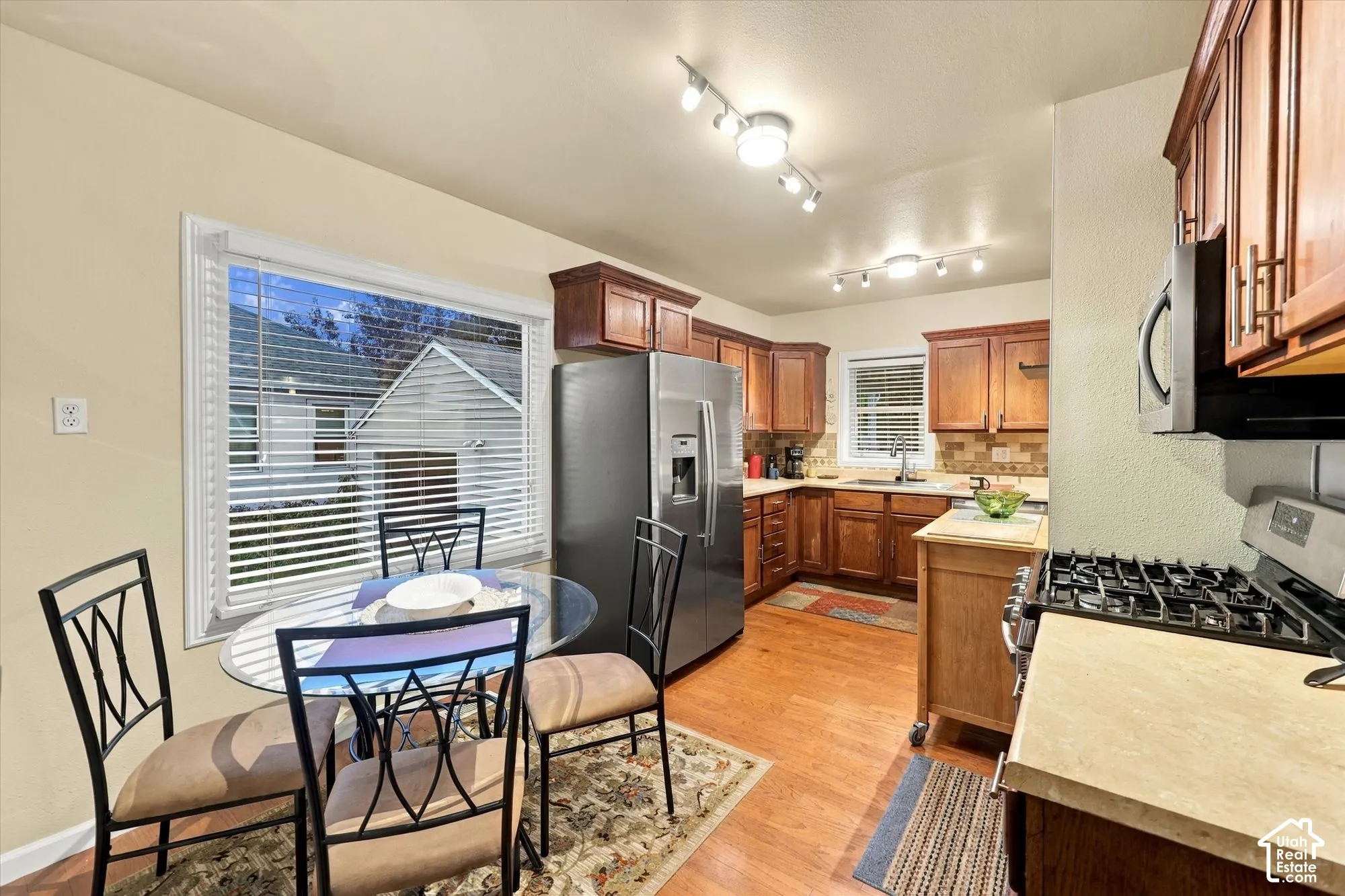 Kitchen featuring wood cabinetry, stainless steel refrigerator, gas range, wood-finish flooring, and multi-bulb track lighting