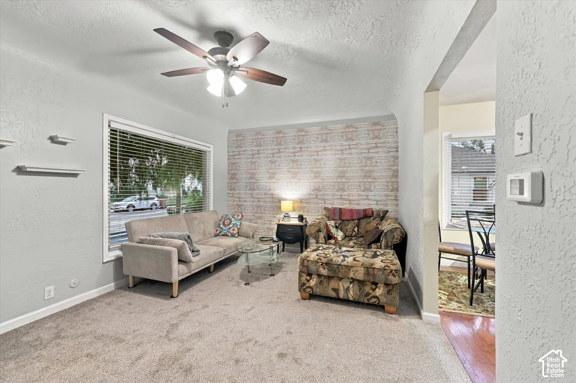 Living area featuring textured wall finish, large window with horizontal blinds, built-in shelving, and a ceiling fan with integrated lighting