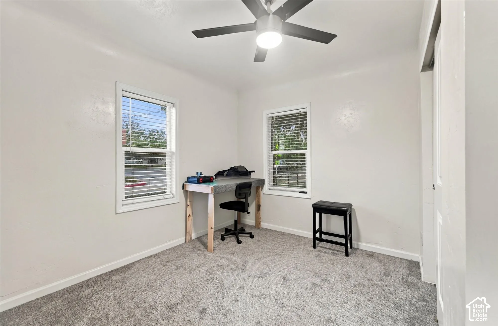 Neutral interior space featuring wall-to-wall carpeting, two dual-pane windows, and a matte black ceiling fan with integrated lighting