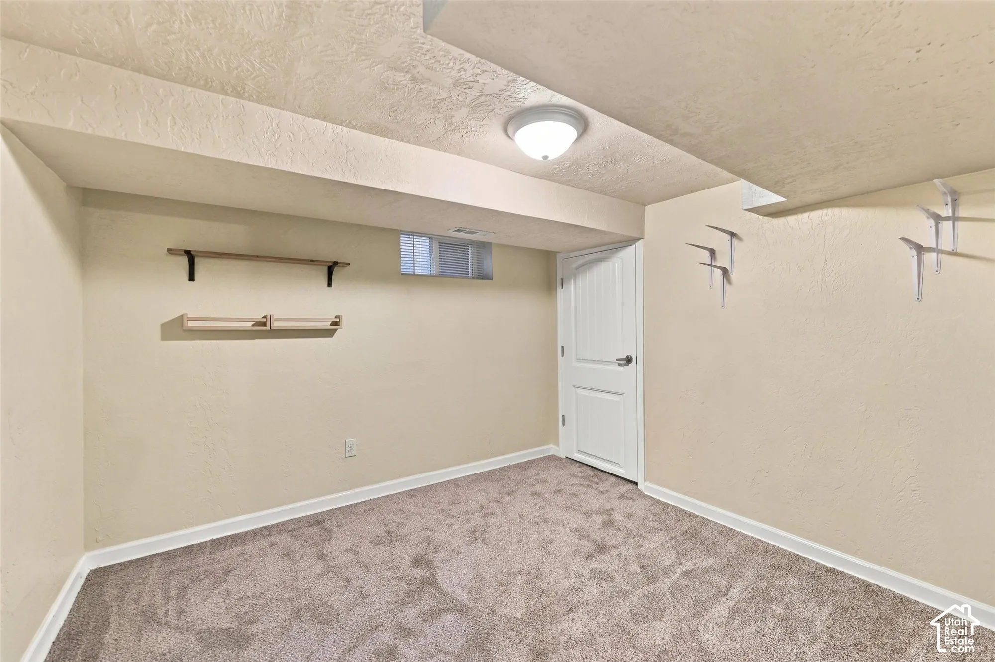Wall-to-wall carpeting, recessed ceiling lighting, single-panel interior door, rectangular hopper window, and multiple wall-mounted shelving brackets