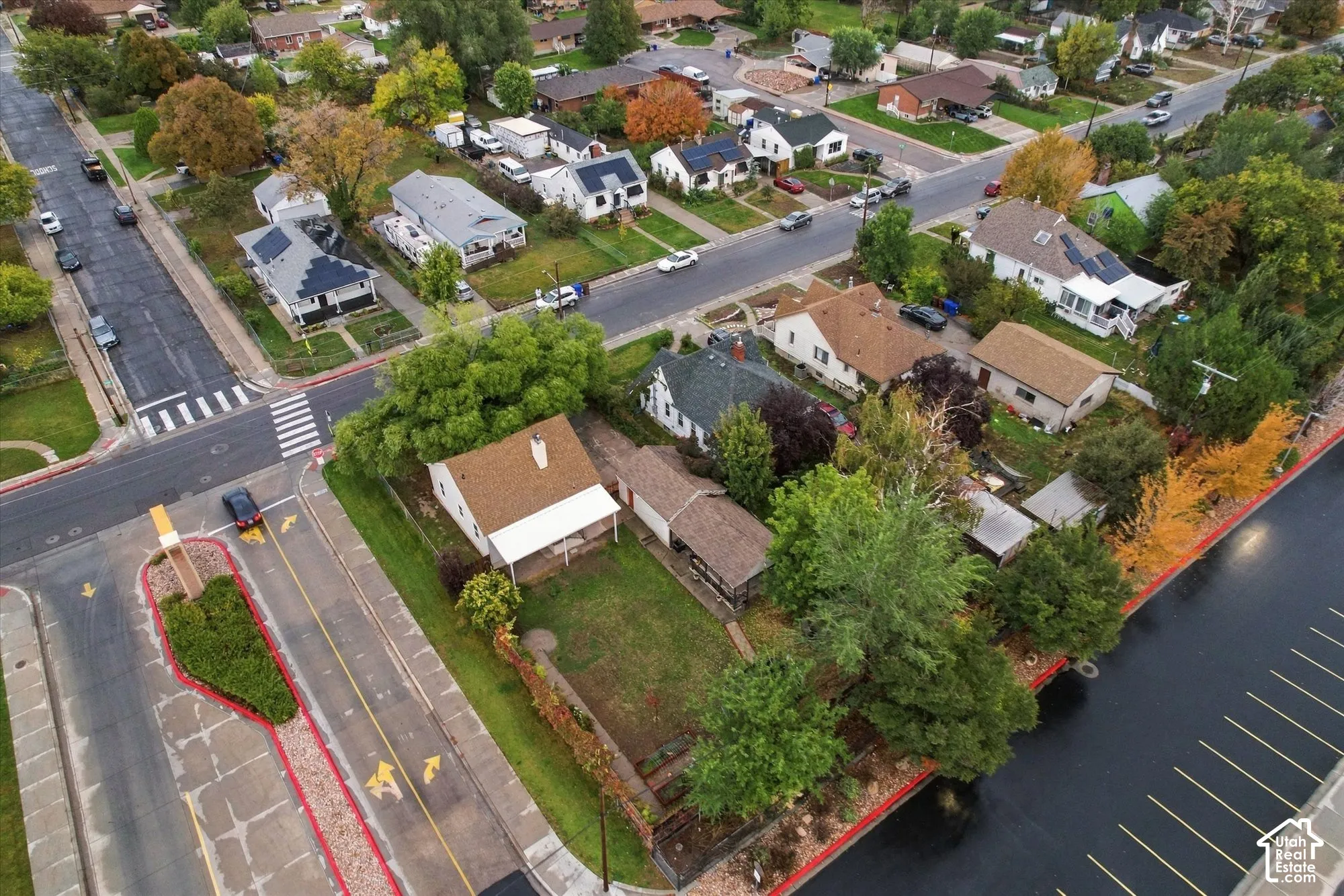 Aerial perspective of a corner lot property featuring a single-story residence, a detached garage, mature trees, and established landscaping