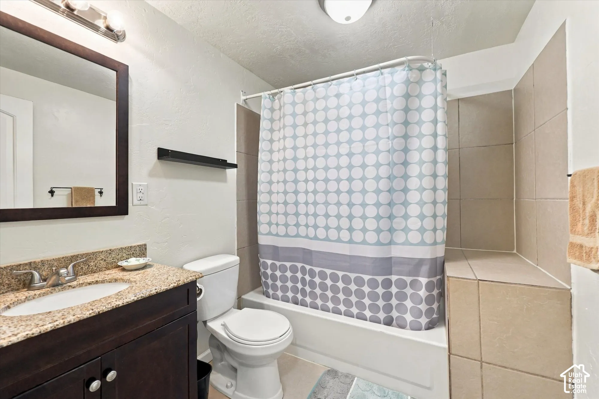 Bathroom featuring a vanity with stone-finish countertop and an integrated oval sink, paired with a shower-tub combination finished with large-format wall tile and a built-in tiled ledge