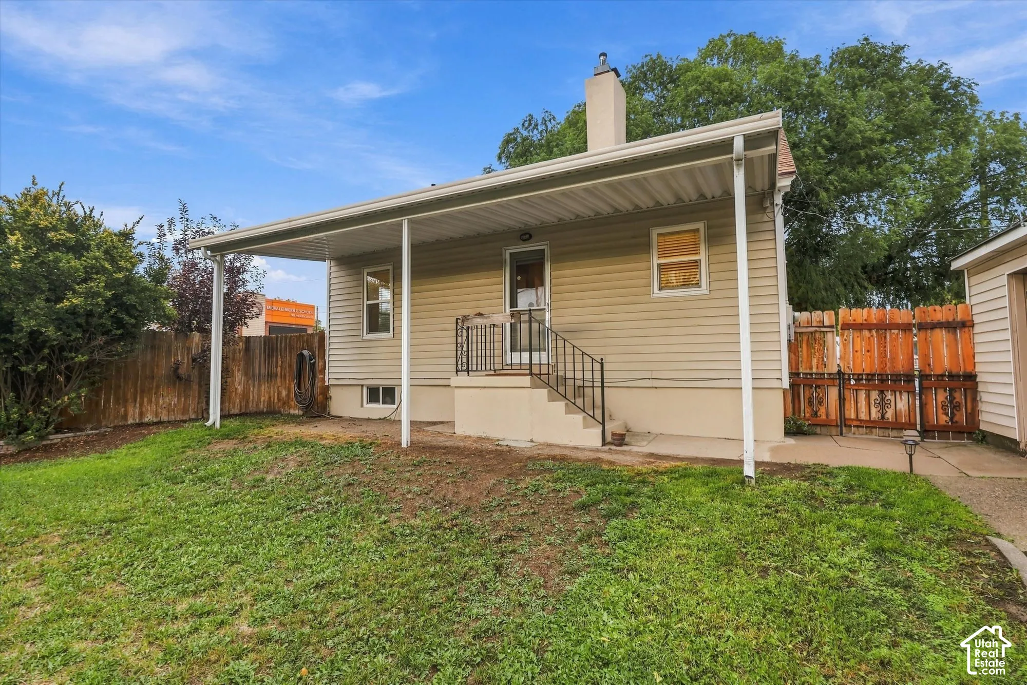 Rear exterior featuring a covered patio, concrete steps with metal railings, a central chimney, and horizontal siding