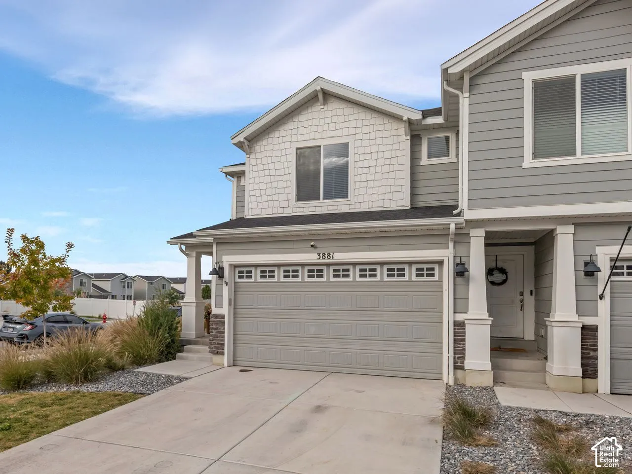 Multi-level exterior featuring grey horizontal lap siding, stone veneer accents, decorative shake siding details, a multi-pane garage door, and white column-supported porch entry