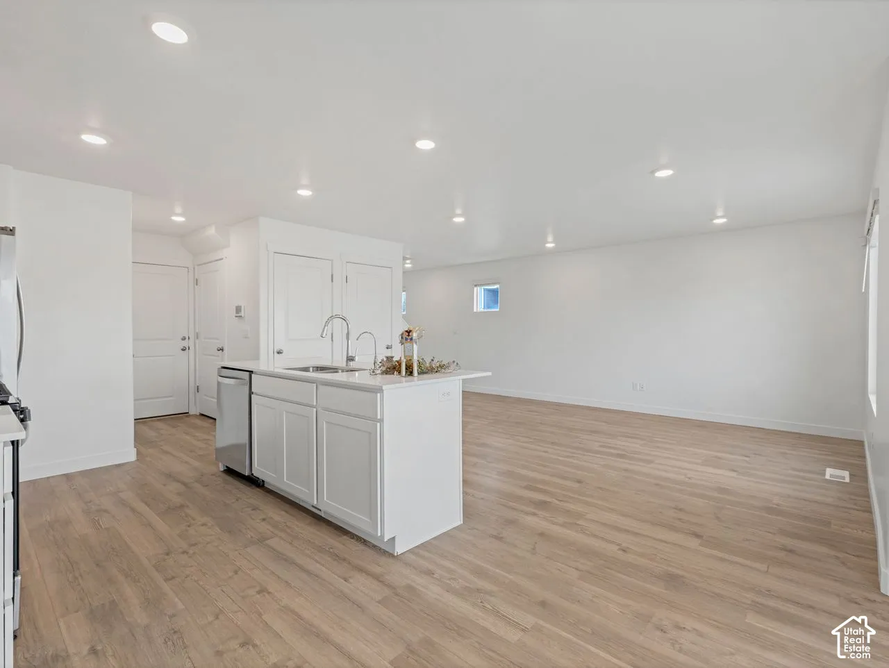 Open-concept interior featuring wood-finish flooring, recessed lighting, and a kitchen island with an integrated stainless steel sink and white cabinetry