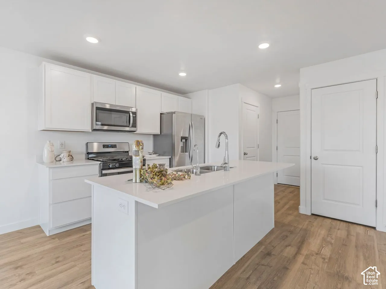 Kitchen featuring white shaker-style cabinetry, a central island with a quartz countertop, stainless steel appliances, and wood-finish flooring