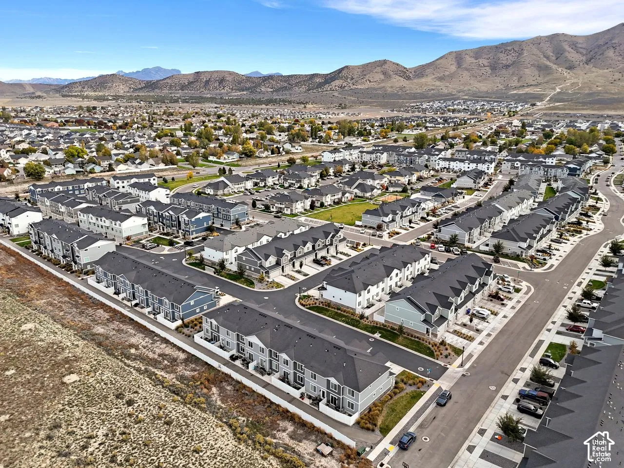 Aerial perspective of a multi-unit residential community featuring asphalt roadways, paved driveways, uniform shingle roofing, and expansive mountain backdrops