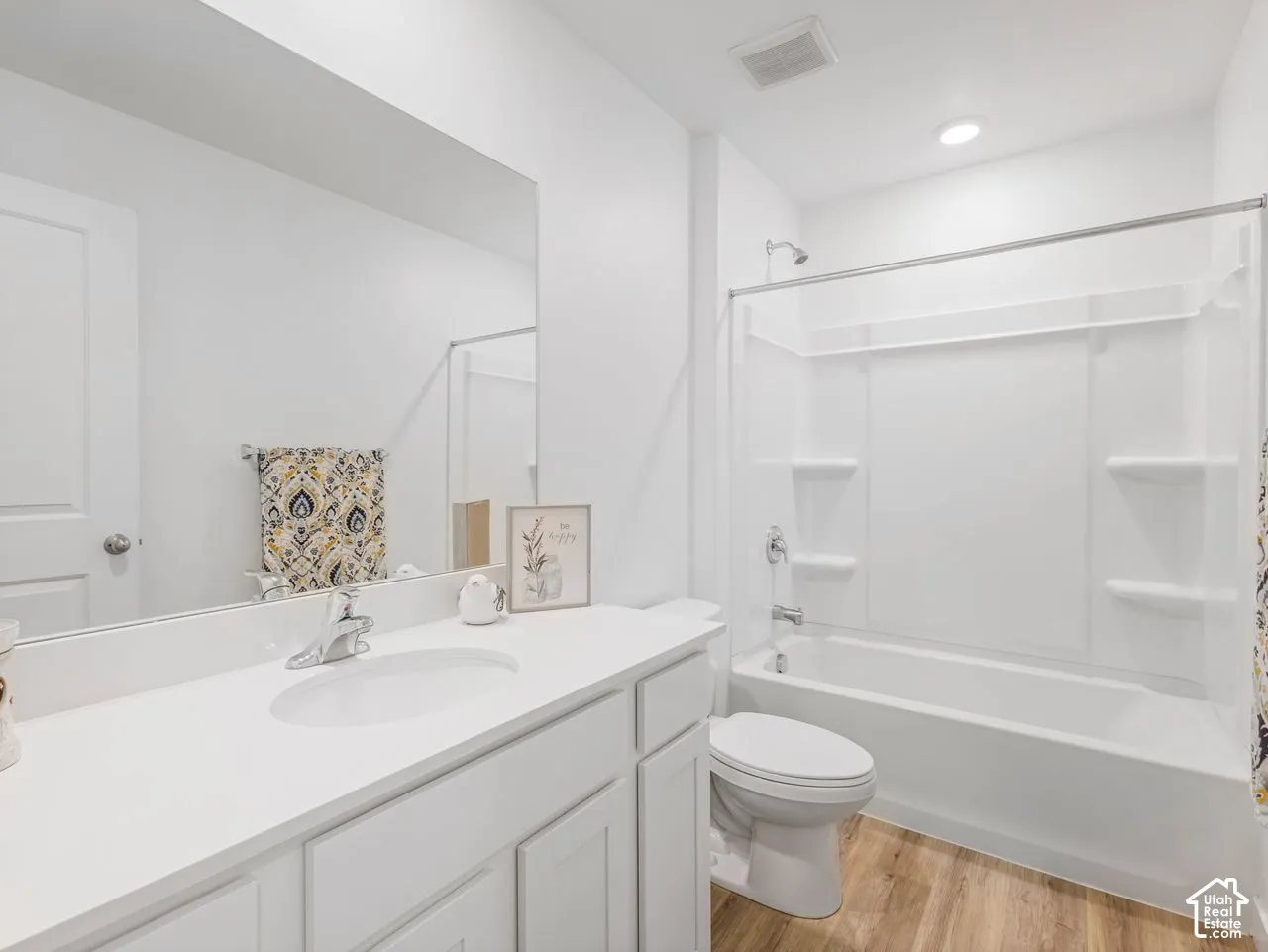 Bathroom featuring a white vanity with a solid-surface countertop, an integrated sink, a full-width wall mirror, wood-finish flooring, and a tub-shower combination with integrated shelving
