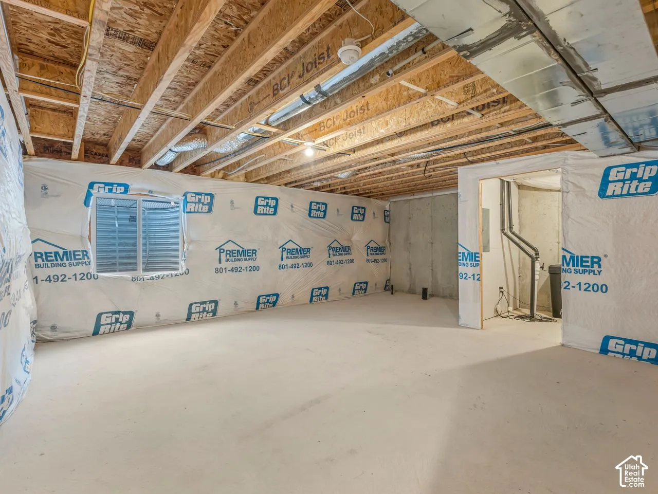 Unfinished lower level featuring exposed engineered wood joists, concrete flooring, foundation walls with vapor barrier wrapping, and an egress window