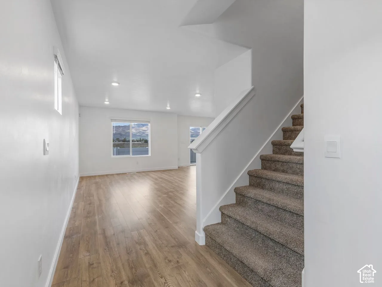 Interior space featuring wood-finish flooring, recessed lighting, carpeted staircase with white handrail, and windows with mountain scenery
