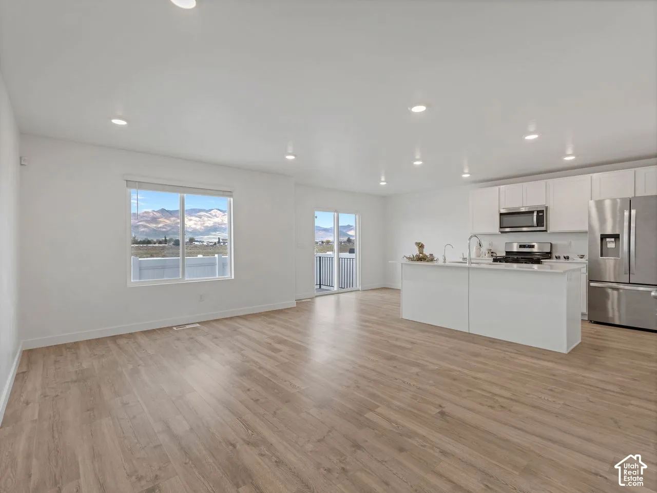 Open-concept space featuring wood-finish flooring, recessed lighting, and a kitchen equipped with white cabinetry, a center island, and stainless steel appliances, highlighted by mountain scenery through the windows