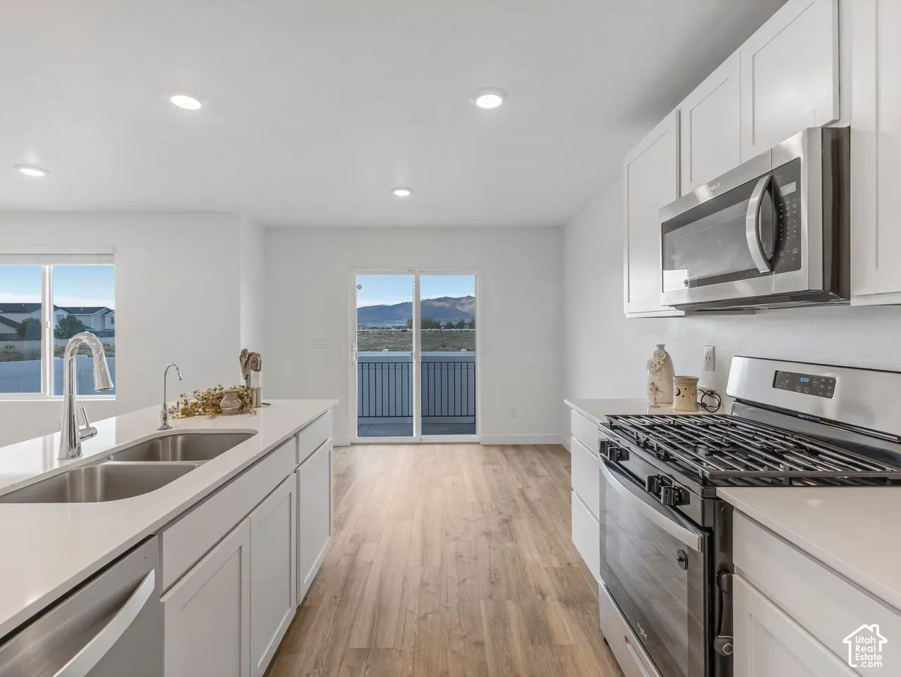Kitchen featuring white shaker-style cabinetry, quartz countertops, stainless steel appliances, dual-basin under-mount sink with pull-down faucet, and wood-finish flooring