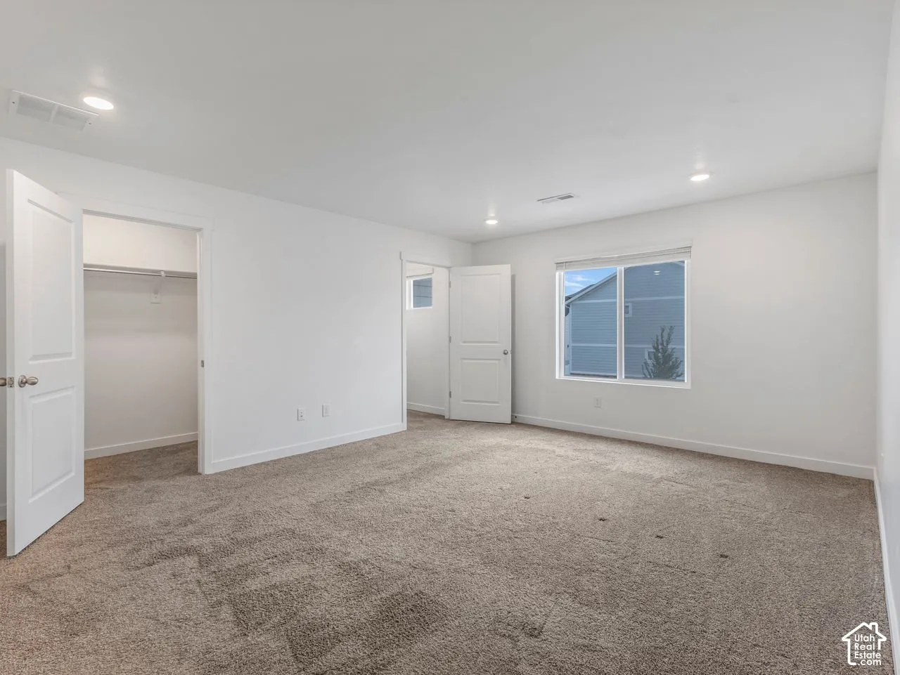 Neutral-toned carpeting, recessed ceiling lighting, sliding window with horizontal blinds, and walk-in closet featuring built-in shelving