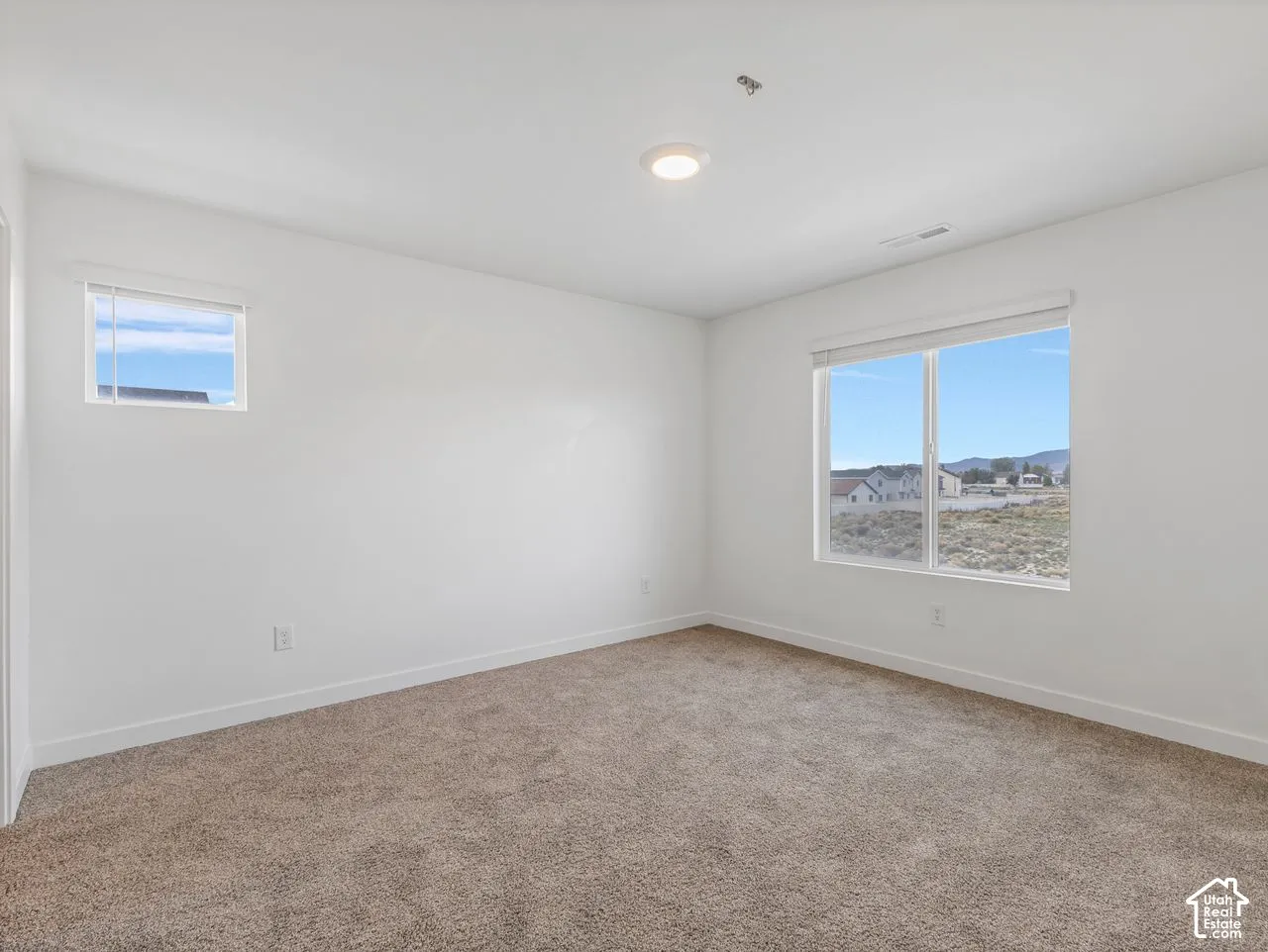 Neutral-toned wall-to-wall carpeting, high-contrast white walls, flush-mount ceiling lighting, and windows featuring exterior mountain and landscape scenery
