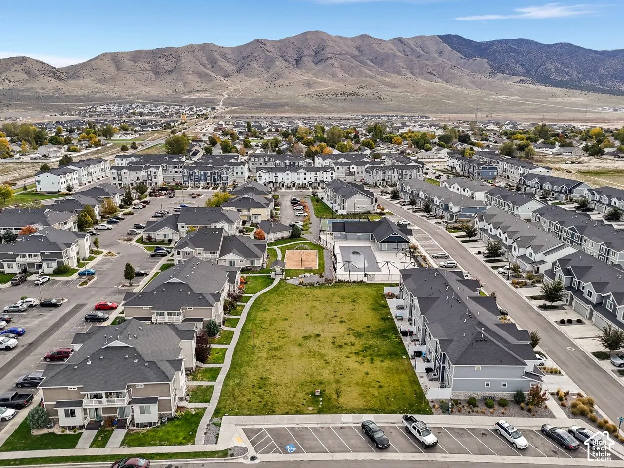 Aerial perspective of residential community featuring a central landscaped common area, swimming pool, pickleball court, and expansive mountain backdrop