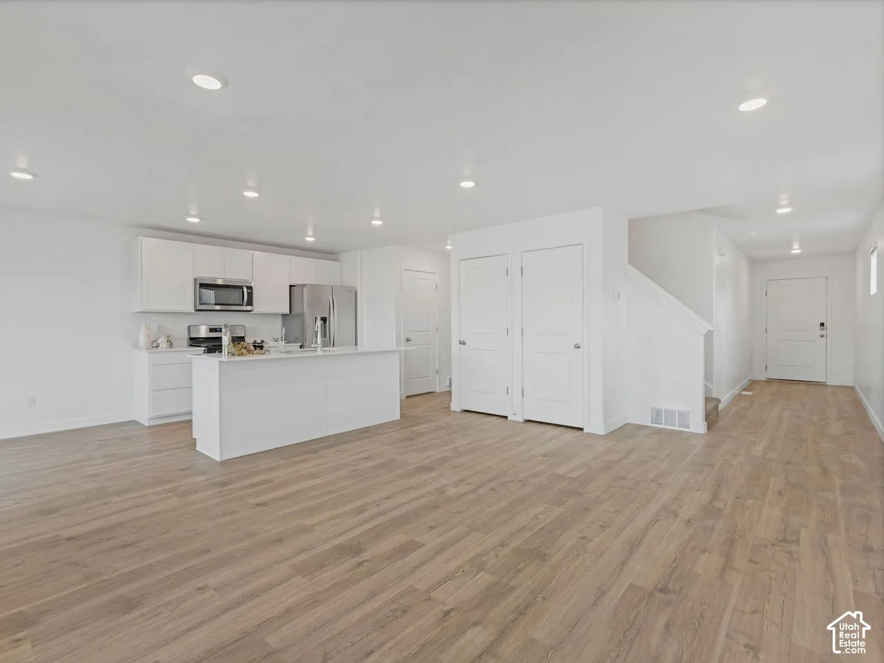 Open-concept living space featuring wood-finish flooring, recessed lighting, white cabinetry, a central kitchen island, and stainless steel appliances
