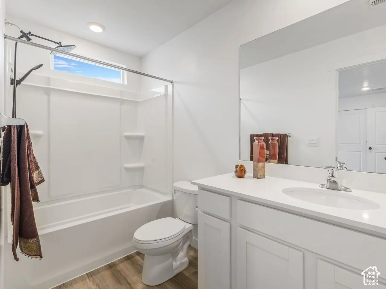 Bathroom featuring a white vanity with an integrated sink, a large wall-mounted mirror, a tub-shower combination with built-in shelving, and wood-finish flooring