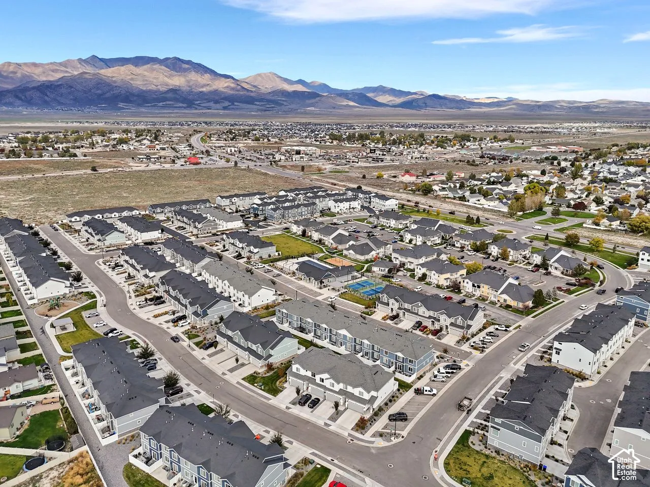 Aerial perspective of residential community featuring multi-family dwellings, paved streets, and expansive mountain scenery