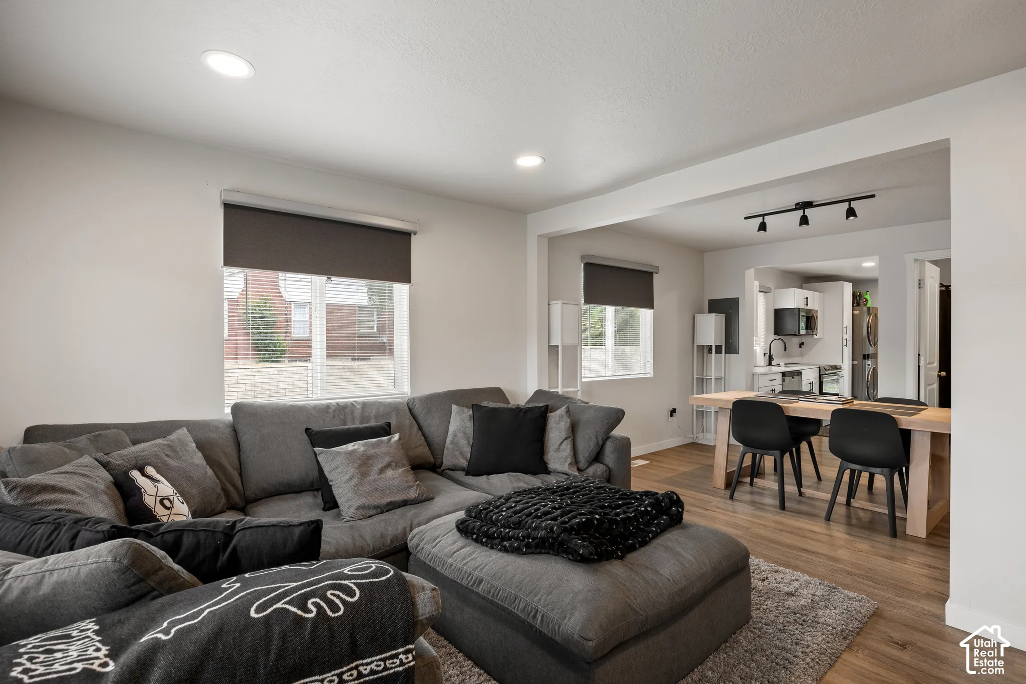 Open living area featuring wood-finish flooring, recessed lighting, and large windows with roller shades