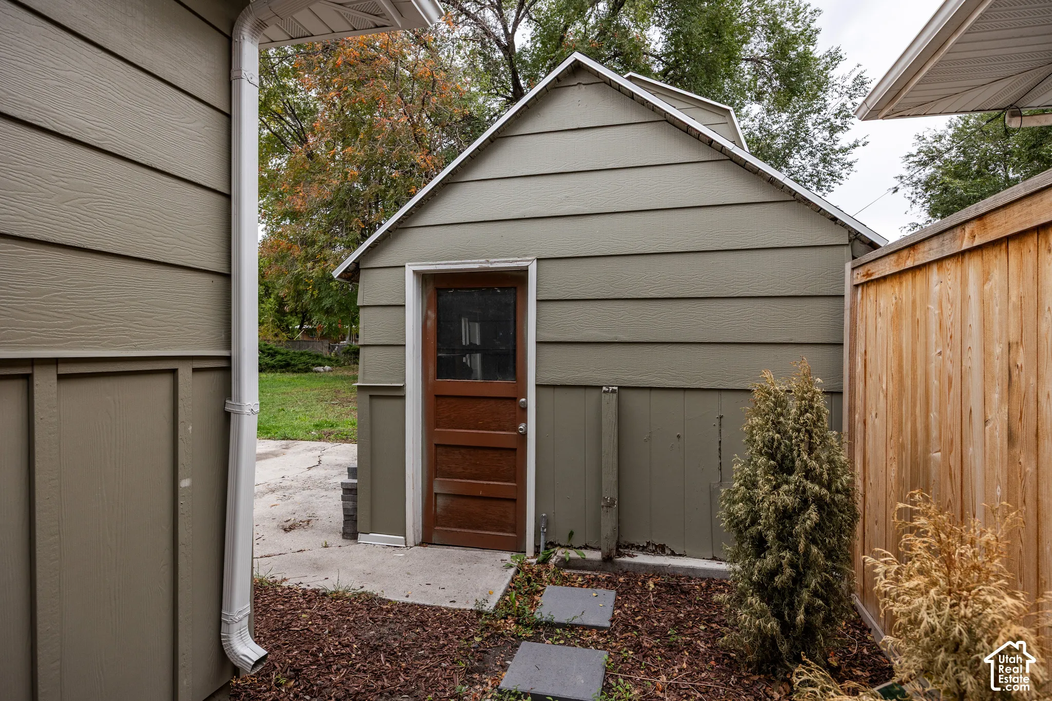 Exterior outbuilding featuring horizontal lap siding, a wood door with a glass inset, and a concrete pathway