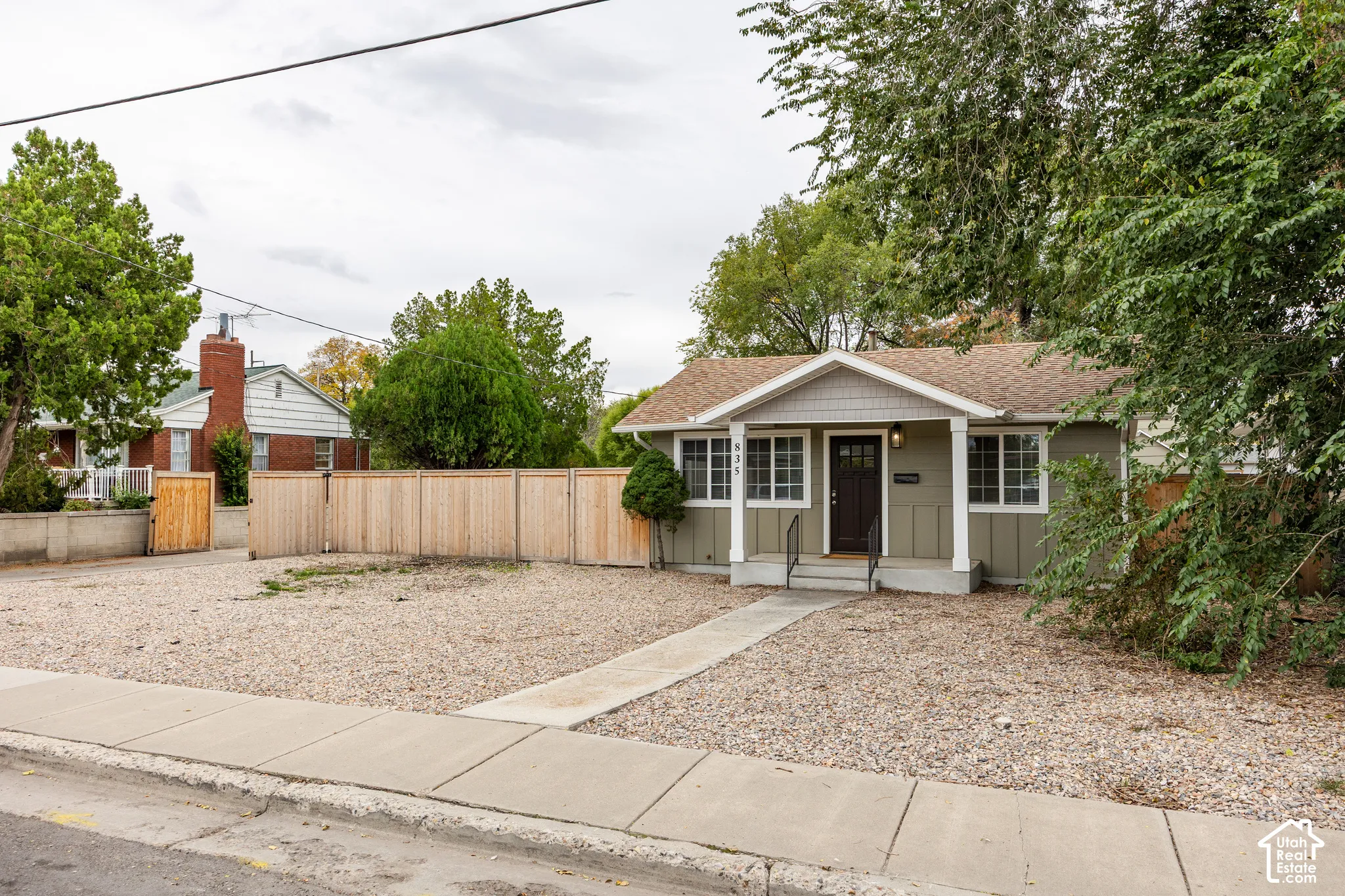 Exterior featuring vertical siding, a covered front porch with a gable roof, wood-finish fencing, a concrete walkway, and gravel landscaping