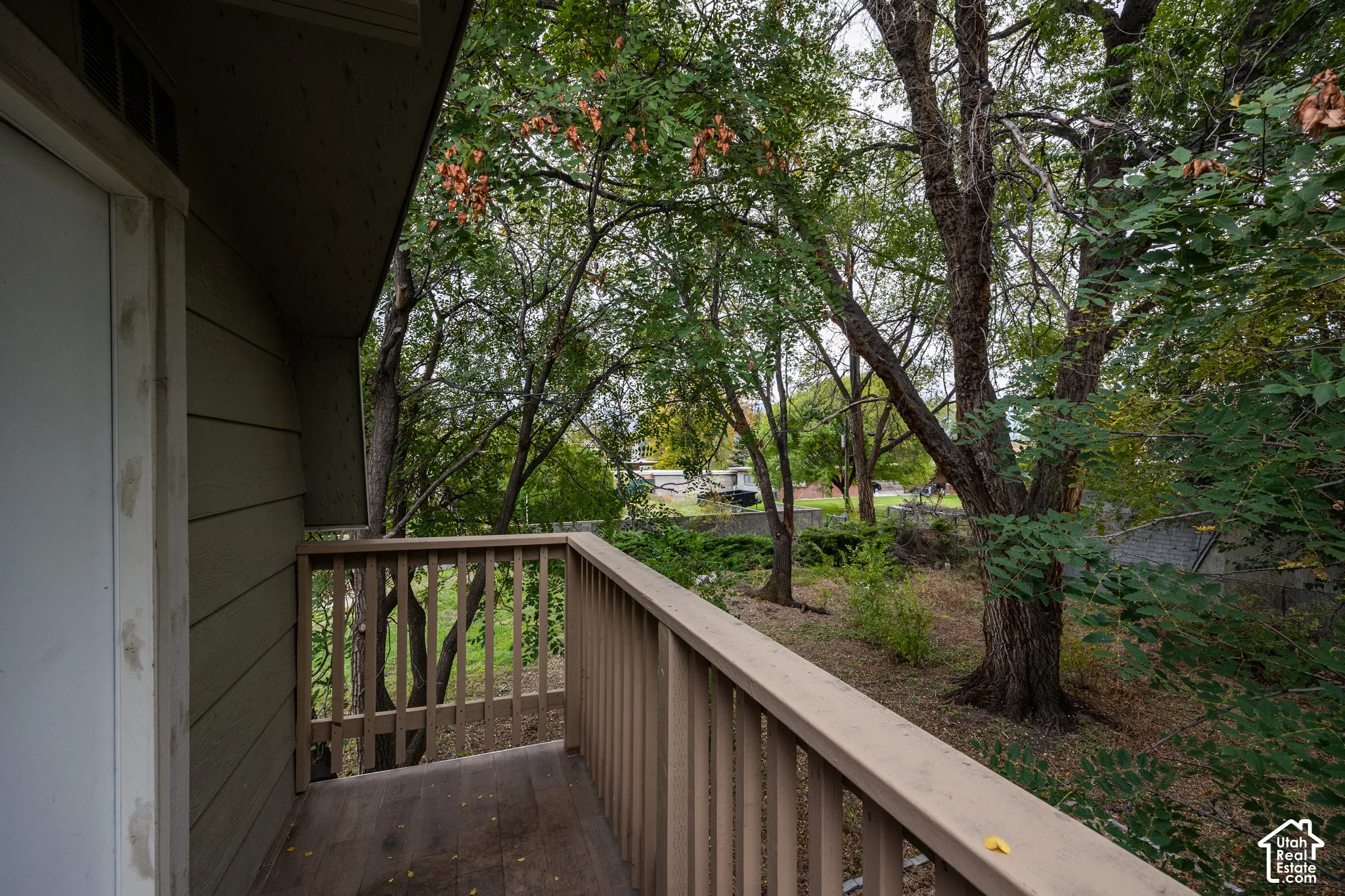 Outdoor balcony featuring wood-finish decking and a wooden balustrade, complemented by mature trees and natural landscaping
